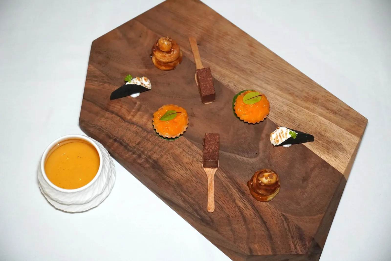 PETIT FOUR ปิดท้าย Petit Four ประกอบไปด้วยขนมเบื้องชาโคลที่มีความหวานจากไส้ฝอยทอง ถัดมาคือทาร์ตส้มจี๊ดที่ประกอบไปด้วยเคิร์ดส้มจี๊ดรสเปรี้ยวท็อปด้วยส้มสายน้ำผึ้ง ชิ้นที่สามคือช็อกโกแลตจากจังหวัดชุมพร สุดท้ายคือโรตีท็อปด้วยน้ำตาบจากรสเค็มและถั่วมาคาเดเมียจากจังหวัดเชียงใหม่ นอกจากนี้ยังมีชาอู่หลงผสมกับโสมเสิร์ฟมาให้อีก 1 แก้วอีกด้วย