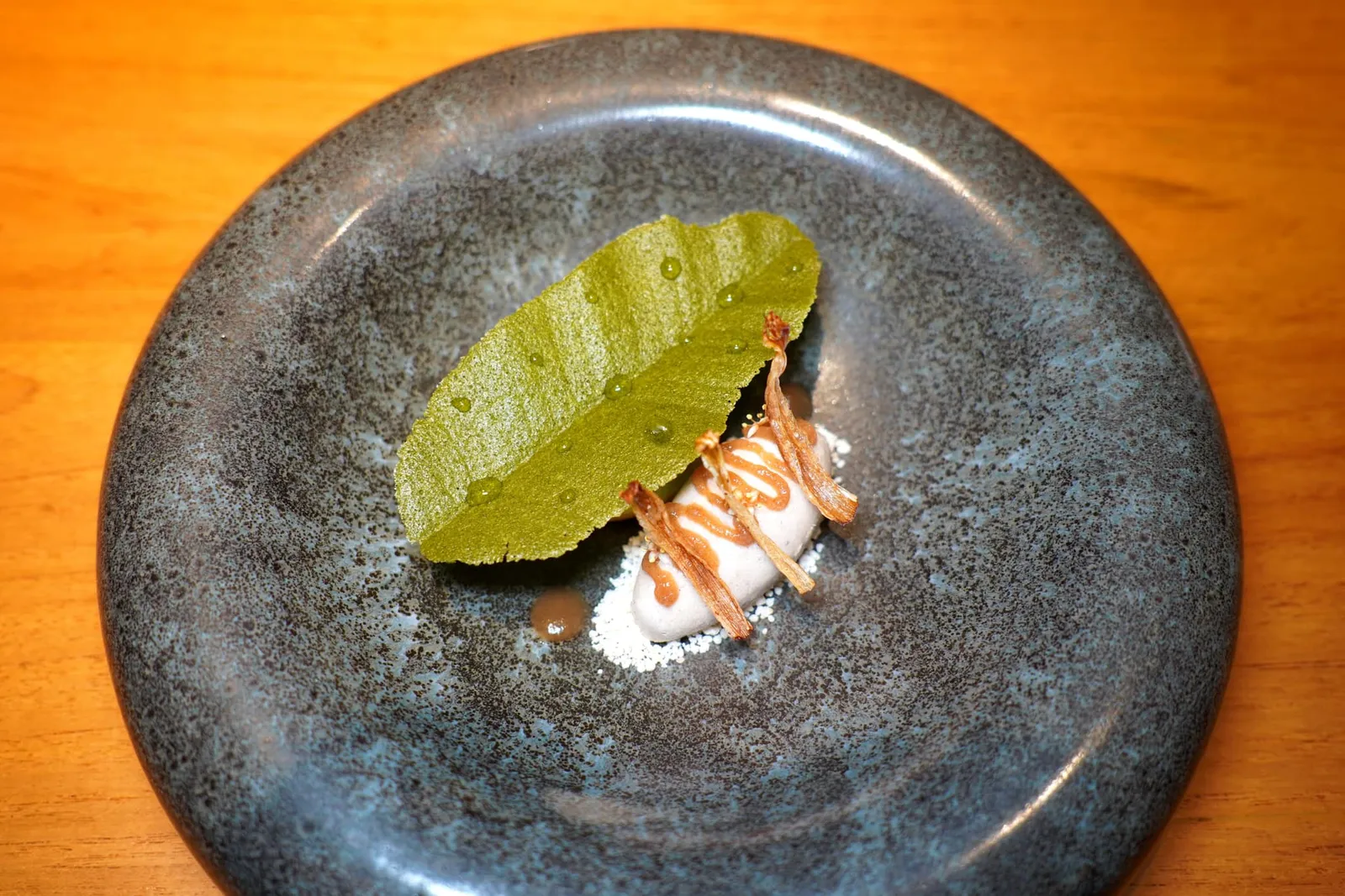 THE BANANA FORESTNAMWAH RAW BANANA | BANANA FLOWERS | BANANA LEAF | DARK RUM | CANE SUGAR | YOUNG GREEN RICE | PANDAN | WHEAT GRASSเค้กอุ่น ๆ เตรียมมาจากข้าวเม่าสดและต้นอ่อนข้าวสาลี จากนั้นท็อปด้วยครีมน้ำนมข้าว ยังมีไอศกรีมกล้วยดิบผสมกับหัวปลีเคี่ยวกับเหล้าดาร์ครัม ด้านบนท็อปด้วยเจลกล้วยตากอบน้ำผึ้งและดอกกล้วยอบกรอบ สุดท้ายคือแผ่นคุกกี้บางกรอบเตรียมมาจากใบตองและใบเตยเสิร์ฟมากับเจลน้ำตาลสด (14/20)