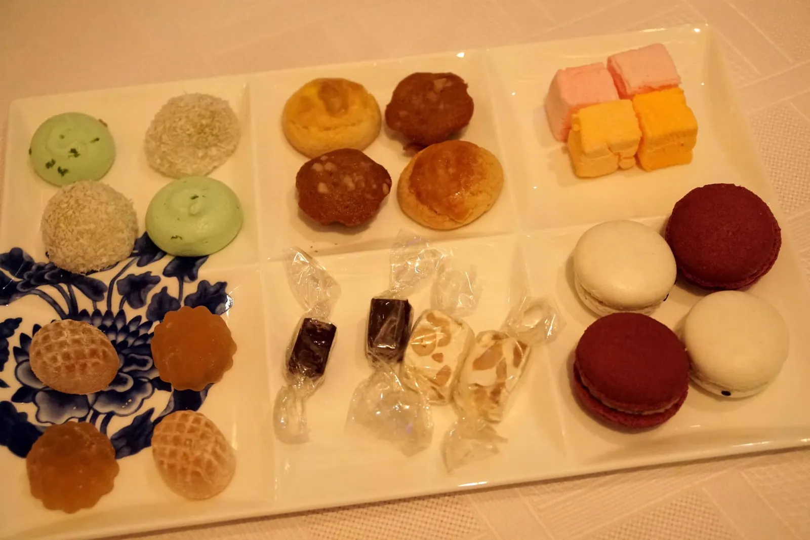 Petit Fours Rose and Orange marshmallow, lychee and passionfruit gummy, ginger caramel chocolate, lime meringue, Macau nougat, glutinous rice roll with lotus seed, red date flavor cake, cashew nut cookies, red bean and black sesame macarons เปอตีโฟว์เซ็ทแรกประกอบด้วยมาร์ชแมลโลว์กุหลาบและส้ม เจลลี่รสลิ้นจี่และเสาวรส ช็อกโกแลตคาราเมลขิง เมอแรงก์มะนาวสีเขียว นูแกตมาเก๊าซึ่งเป็นขนมหวานพื้นบ้านของที่นี่ แป้งสอดไส้เมล็ดบัว ขนมเค้กพุทราจีน คุกกี้เมล็ดมะม่วงหิมพานต์ มาการองถั่วแดงสีแดงเเละมาการองงาดำสีขาว (12/20)
