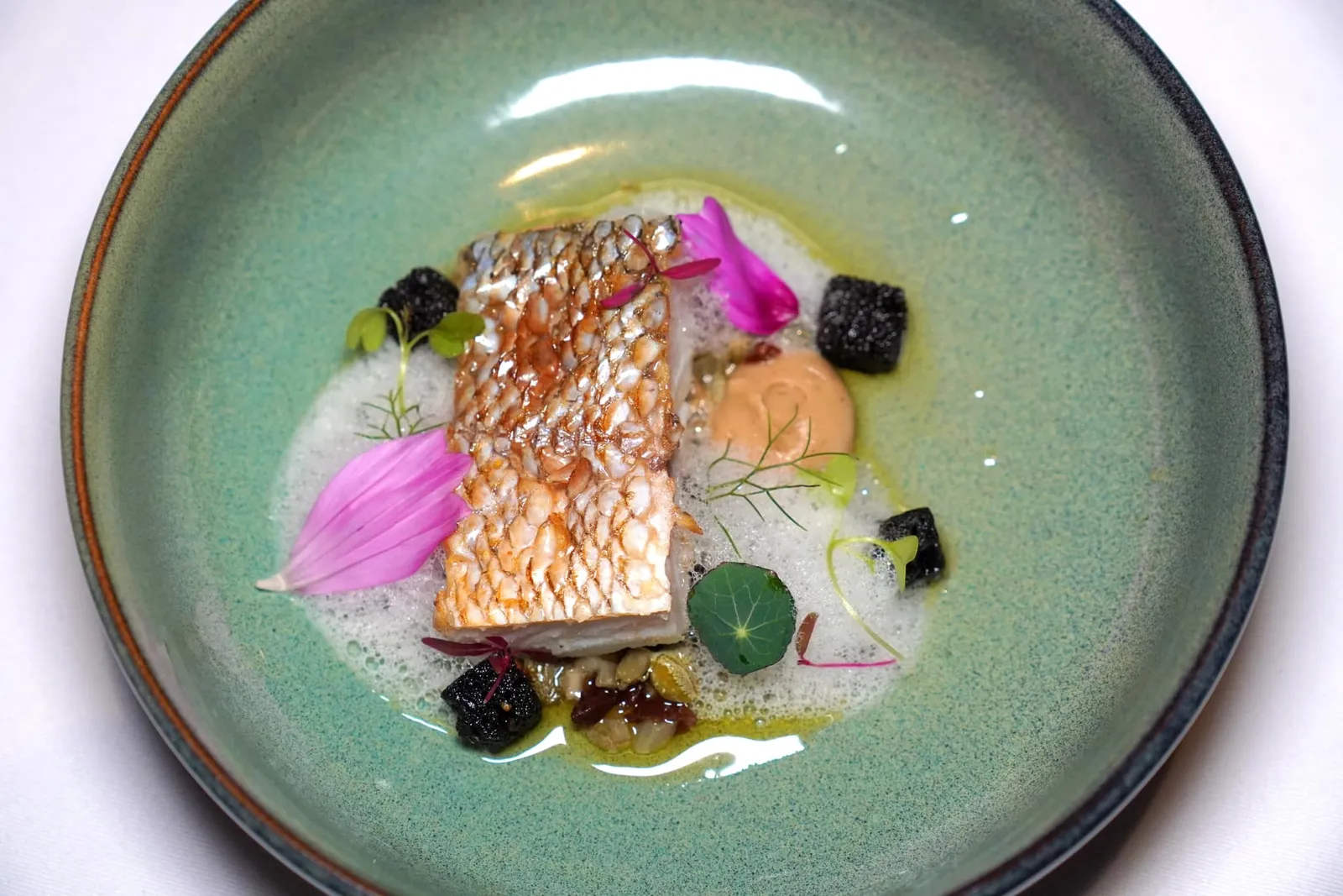 Wild Caught Barracuda Celeriac Cremeux, Grenobloise, Squid Inked Crûtons, Beurre Noisette, Fish Foam เมนคอร์สจานปลาเชฟเลือกใช้ปลาน้ำดอกไม้เสิร์ฟมากับขนมปัง Crouton ที่มีสีดำจากดีหมึกตัดเนื้อสัมผัสกันอย่างลงตัว ด้านล่างมีความหวานมันของซอส Beurre Noisette ตัดด้วยความฉุนเบา ๆ ของครีมเซเลอรี่ จากนั้นจึงจบด้วยการเติมแต่งโฟมสีขาวที่เตรียมขึ้นมาจากน้ำสต็อกปลา เกล็ดปลา และกระดูกปลา (14/20)