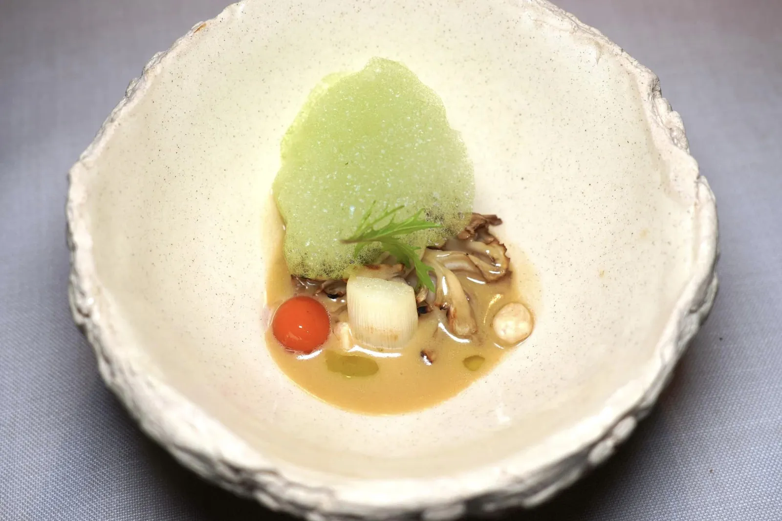 White asparagus, grilled Maitake, soft pickled mushroom cream and sobrasada หน่อไม้ฝรั่งขาวทั้งส่วนต้นและส่วนยอดวางมาเคียงข้างกันกับเห็ดไมทาเกะ องค์ประกอบทั้งคู่ผ่านการย่างจนสุกพอดีแล้วเสิร์ฟมากับครีมนุ่ม ๆ ที่เตรียมมาจากเห็ดดอง ถั่วฮาเซลนัท ด้านบนคือโฟมสีเขียวที่เตรียมมาจากพาสลีย์ ยังมีสเฟียร์สีส้มแดงที่เตรียมมาจาก Sobrasada หรือไส้กรอกหมูหมักท้องถิ่นให้รสเปรี้ยวที่โดดเด่นนั่นเอง (18/20)