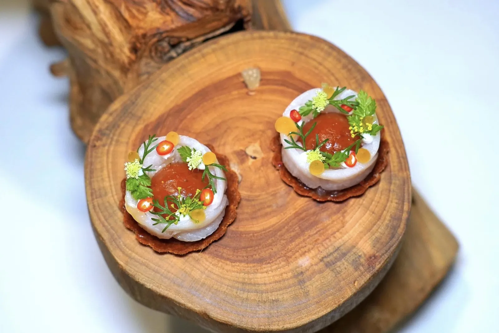 CATCH OF THE DAYRed Curry, Finger Lime, Citrusของว่างที่หยิบยกเมนูปลาผัดพริกขิงและพล่าปามาผสมผสานไว้ในจานเดียวกัน ด้านล่างเป็นทาร์ตแป้งบางกรอบที่มีส่วนผสมของเครื่องแกงผัดพริกขิง ด้านในมีเครื่องยำแอบซ่อนเอาไว้ ตรงกลางคือ Aspic Jelly ที่เตรียมมาจากน้ำพล่าให้ความจัดจ้านเสริมด้วยความเปรี้ยวของมะนาวนิ้วมือ เนื้อปลาช่อนทะเลผ่านการบ่มกับสาหร่ายคอมบุญี่ปุ่น เชฟนำมาแล่แล้ววางเรียงกันมาอย่างสวยงามและให้เนื้อสัมผัสที่นุ่มกว่าแป้งทาร์ตได้อย่างมีมิติ จากนั้นท็อปด้านบนด้วยสมุนไพรสด เพียวเรมะพร้าว และพริกซอย (15/20)
