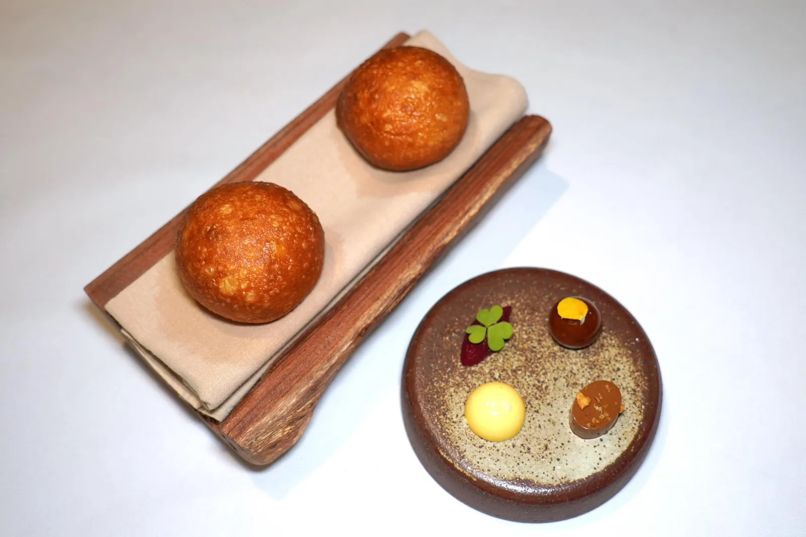BREAD & BUTTERSour Soy Sauce, Torch Ginger, Local Herbsขนมปัง Signature Bread เชฟได้รับแรงบันดาลใจมาจากซาลาเปาทอด ขนมจีบ และขนมไข่นกกระทา เชฟเสิร์ฟมาร้อน ๆ โดยมีส่วนผสมของมันฝรั่งบดอยู่ด้วยแล้วค่อยนำไปทอดเพื่อให้มีเนื้อสัมผัสที่โดดเด่นและคุ้นเคย เครื่องจิ้มขนมปังมี 4 อย่างเริ่มจากเนยที่มีอโรมาหอม ๆ ของจิ๊กโฉ่วซึ่งผ่านการเคี่ยวจนงวดแล้วท็อปด้านบนด้วยกระเทียมเจียวชวนนึกถึงขนมจีบแบบไทย ข้าง ๆ กันคือเนยนำเข้าจากประเทศฝรั่งเศสโรยด้วยเกลือหวานจากจังหวัดปัตตานี ถัดมาคือชัทนีย์ดอกดาหลาที่ได้จากการนำดอกดาหลาไปผัดกับบีทรูทและน้ำส้มข้าว สุดท้ายคือน้ำพริกที่ได้จากการนำพริกหลายชนิดไปเผาแล้วผสมกับกุ้งแห้งแล้วเคลือบด้วยอาจาดนั่นเอง (15/20)