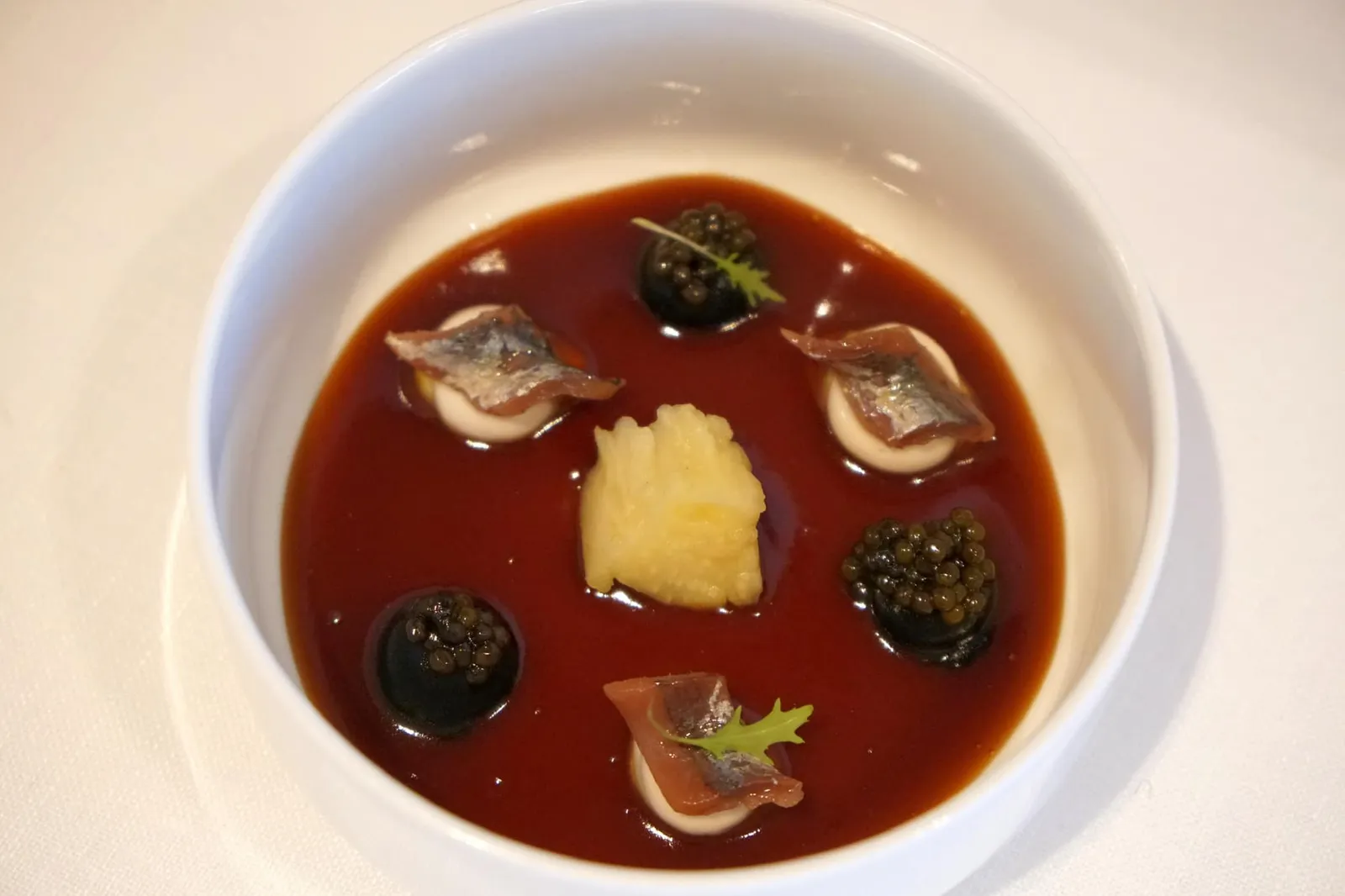 Roasted EGGPLANT, anchovy, caviar and legume broth หลังจากนำมารวมกันจะไปอาหารจานถัดไปคือ Roasted Aubergine & Eggplant เริ่มจากองค์ประกอบแรกคือ Roasted Eggplant ที่ย่างมาสุกกำลังดี พนักงานจะคัดเฉพาะส่วนบริเวณที่เนื้อนุ่ม หวาน ทานเเล้วมีกลิ่นหอมจากการย่าง ด้านล่างคือสตูว์ทำจาก chickpea หรือถั่วลูกไก่ที่เชฟนำไปรีดัคชั่นเป็นระยะเวลากว่า 48 ชั่วโมงจนงวด มีสีคล้ายคาราเมล มีรสชาติเข้มข้น ถัดมาคือ Emulsion สองสี เริ่มจากสีดำทำจากผิวของมะเขือเผา (Skin of Roasted Aubergine) ทอปด้านบนด้วย Beluga caviar ส่วนสีขาวคือ Anchovy Emulsion ทอปด้านบนด้วย Anchovy ชิ้นเล็กๆที่ได้มาจากเมือง Bermeo โดย Bermeo Anchovy เป็นสินค้าท้องถิ่นที่สำคัญของภูมิภาค Basque Country ทำจากปลาขนาดเล็กที่จับมาจาก Bay of Biscay ด้านบนคือคือใบ Mizuna leaf มีรสชาติเเละเนื้อสัมผัสคล้าย Baby rocket เพิ่มความสดชื่นเล็กน้อยให้กับจาน (20+/20)