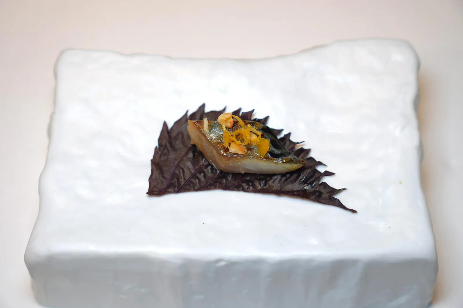 Amuse-bouche ถัดมาคือใบชิโสะจับคู่มากับกลิ่นอายทะเลที่ได้จากปลาแมคเคอเรลย่าง ทั้งยังมีเนื้อสัมผัสสู้ฟันพอเหมาะ นอกจากนี้ยังมีรสชาติของส้มและความกรอบของถั่วฮาเซลนัทอีกด้วย เชฟแนะนำให้ห่อรับประทานทั้งหมดในคำเดียว (18/20)
