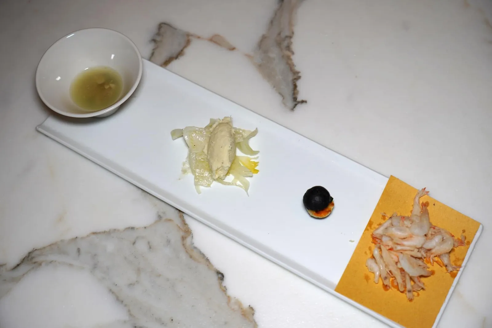 Amuse-bouche เริ่มต้นมื้ออาหารด้วยของว่างเรียกน้ำย่อยประกอบไปด้วยกุ้งฝอยทอดกรอบ เคี้ยวง่าย ไม่อมน้ำมัน รสชาติออกเค็มนิด ๆ ข้างกันคือเบอร์เกอร์สีดำชิ้นจิ๋ว ตรงกลางคือเนื้อของหมึกหนึบ ๆ ผักปวยเล้ง และซอสมะเขือเทศ ถัดมาคือครีมปลาค็อดเนื้อสัมผัสละมุนคล้ายสำลีเสิร์ฟมาคู่กันกับเฟลเนล สุดท้ายคือเซวิเช่เสิร์ฟมากับหอยลายอิตาลีและคาเวียร์ (14/20)