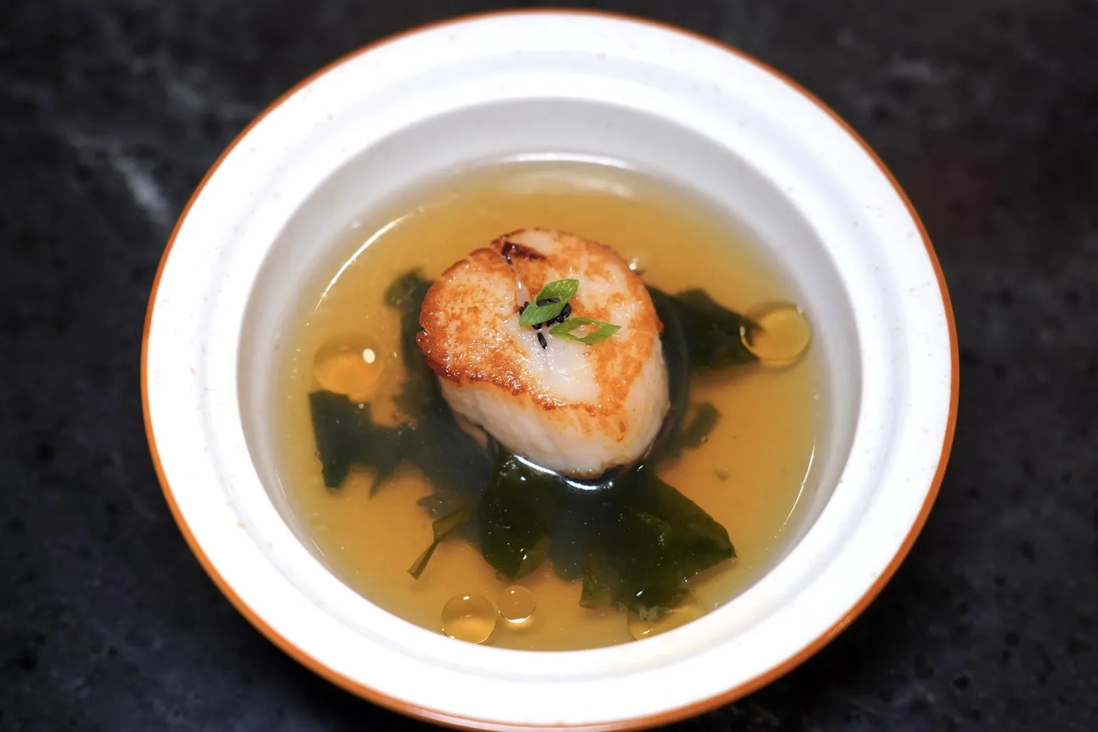 SCALLOP MIYEOK CONSOMME 가리비 미역 큰소메 เชฟตั้งใจนำเสนอ Miyeok-guk หรือซุปสาหร่ายที่นิยมรับประทานกันในประเทศเกาหลีโดยเฉพาะในช่วงวันเกิดเพื่อระลึกถึงคุณแม่ เชฟนำเสนอมาในลักษณะของซุปใสรสชาติกลมกล่อมอุมามิ เชฟเพิ่มมิติทางเนื้อสัมผัสด้วยความแตกต่างของสาหร่ายและเห็ดหอม ด้านบนท็อปด้วยหอยเชลล์ที่ผ่านการ Dry-aged นาน 5 วันก่อนจะนำมาเซียร์มาจนสุกกำลังดี เนื้อหอยมีความเฟิร์มมากกว่าปกติ จากนั้นเพิ่มความหอมด้วยการหยดน้ำมันงาเกาหลีลงไปในช่วงที่จัดเสิร์ฟ (15/20)