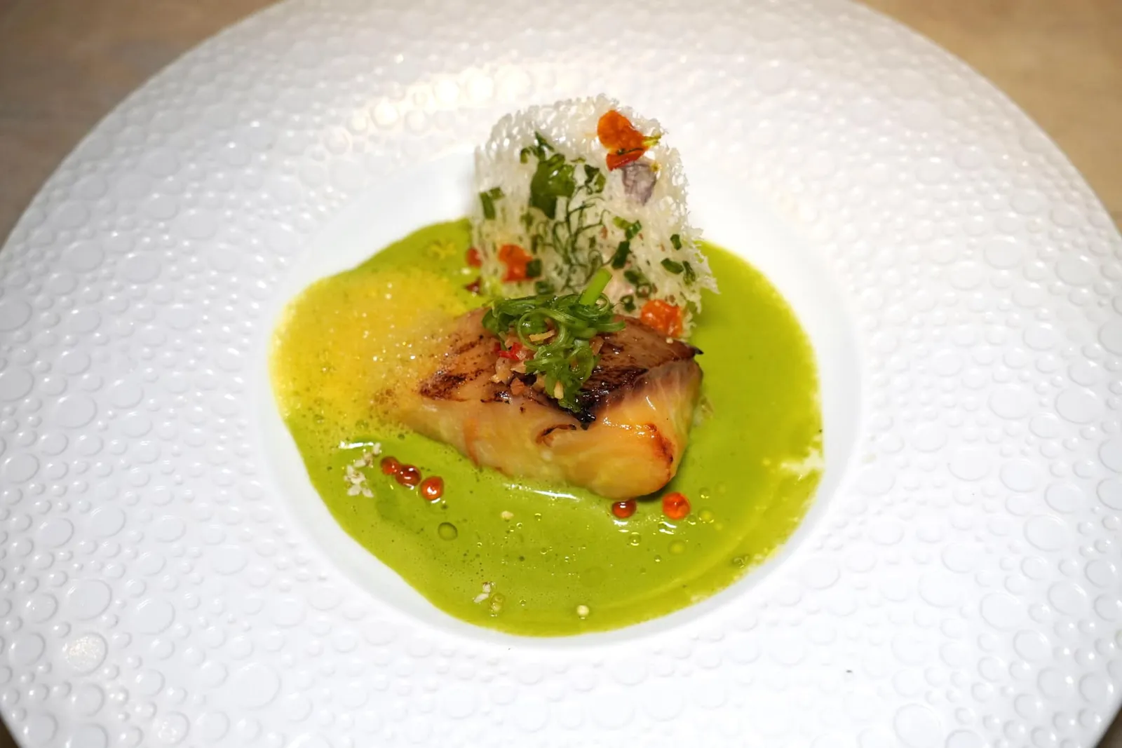 CHẢ CÁ HÀ NỘIBlack cod, turmeric and local dill cream sauceChả Cá Lã Vọng เป็นเมนูที่นำเสนอปลาดุกคลุกเคล้ามาคู่กันกับขมิ้นและผักชีลาว ในที่นี้เชฟได้เปลี่ยนมาใช่ปลาแบล็คค็อดเพื่อให้มีเนื้อสัมผัสที่ละมุนลิ้นมากขึ้น นอกจากนี้ยังมีซอสครีม Thì Là หรือผักชีลาวของเวียดนามเสริมกันกับอโรมาเบา ๆ ของขมิ้นและหัวหอม เชฟเพิ่มความกรุบกรอบด้วยการใส่ไข่ปลาแซลมอนลงมาด้วย สุดท้ายคือแผ่นกรอบที่เตรียมมาจากเส้น Bun ปรุงรสด้วย Mắm Tôm ที่มีลักษณะคล้ายกันกับกะปิ (14/20)
