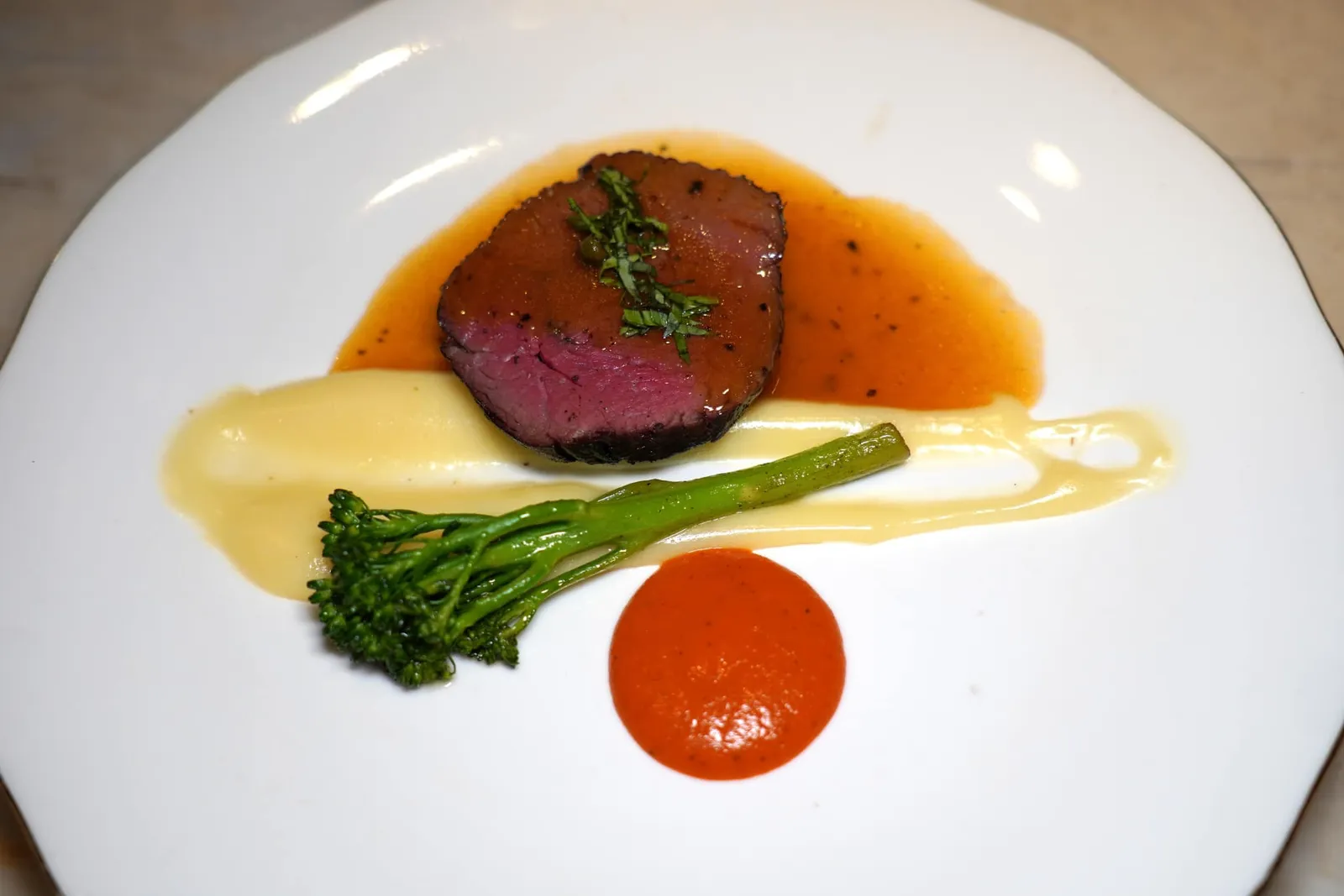 SAIGON SHAKING BEEFPremium Black Angus, mashed potato, Phú Quốc pepper sauceMain Course ในวันนี้เชฟอาศัยแรงบันดาลใจมาจาก Bò Lúc Lắc หรือเมนูที่เรียกกันว่า Shaking Beef สไตล์ Saigon อันเนื่องมาจากพ่อครัวจะทำการเขย่ากระทะที่มีเนื้อหั่นเต๋าจนชิ้นเนื้อกลิ้งไปมาและเกิดกระบวนการ Maillard Reaction ด้วยความที่เป็นเมนูที่ได้รับแรงบันดาลใจมาจากอาหารฝรั่งเศสทำให้คนเวียดนามนิยมรับประทานเมนูนี้ควบคู่ไปกับ French Fries หรือขนมปัง Baguette ในที่นี้เชฟเปลี่ยนมาใช้เนื้อวัว Australian Wagyu ส่วนสันในจี่แล้วเสิร์ฟมาที่ความสุกระดับ Medium Rare จากนั้นราดด้วย Brown Butter ข้างกันคือ Mashed Potato เนื้อเนียนและซอสพริกไทยบดจากเกาะ Phú Quốc (13/20)