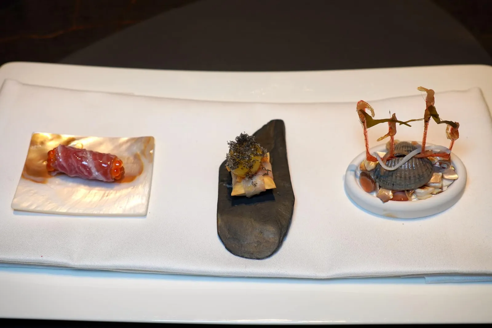 Daily OfferOur chef Thomas Schanz has created a versatile menu using the best ingredients.เริ่มต้นมื้ออาหารด้วยของว่างเรียกน้ำย่อย 3 อย่าง ฝั่งขวามือสุดคือแผ่นกรอบที่เตรียมมาจากกุ้งจิ๋วโดยมีกลิ่นหอมที่ได้จาก Lardo หรือไขมันสัตว์และเมลอน ถัดมาตรงกลางคือ Blanket หรือหมอนกรอบ ๆ จับคู่กับรสชาติของปลาไหลรมควัน ด้านบนคือองค์ประกอบของไข่แดงและไข่ปลาเพิ่มความมันและอุมามิ ชิ้นสุดท้ายคือ Cannelloni ที่ห่อด้วยเนื้อปลาทูน่าและปิดหัวท้ายด้วยไข่ปลาเทร้าต์ (18/20)
