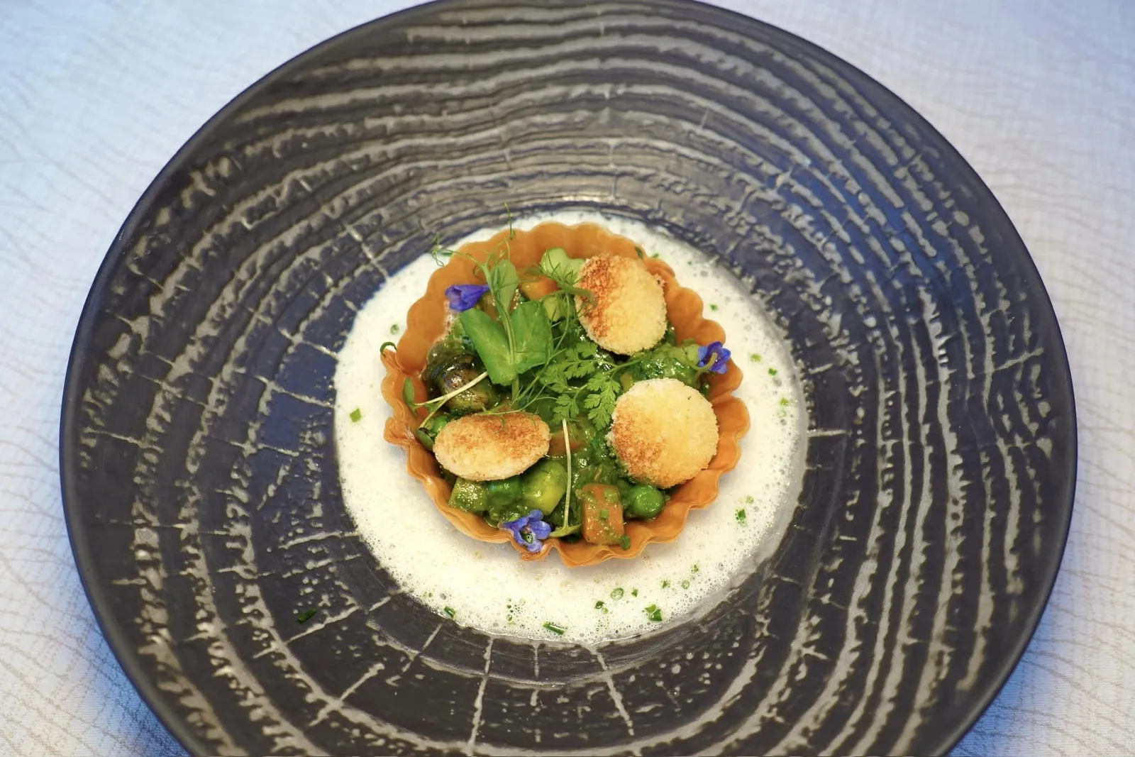 Fine tartelette croustillante d'escargots, fèves, petits pois et légumes de saison, infusion de lard paysan, pain de mie toastéTartelette แผ่นบางที่ภายในบรรจุองค์ประกอบหลากหลายทั้งหอยทาก ถั่ว และผักตามฤดูกาลนานาชนิด ชิ้นหอยทากนุ่มหนึบพอเหมาะและไม่มีกลิ่นดินที่มากจนเกินไป เชฟใส่อโรมาของ Lard หรือไขมันสัตว์ลงไปด้วย ยังมีองค์ประกอบของครูตรองกรอบ ส่วนซอสสีเขียวเตรียมมาจากใบเบซิลช่วยบาลานซ์กลิ่นเฉพาะตัวของหอยทากได้อย่างไร้อย่างไรที่ติ (16/20)