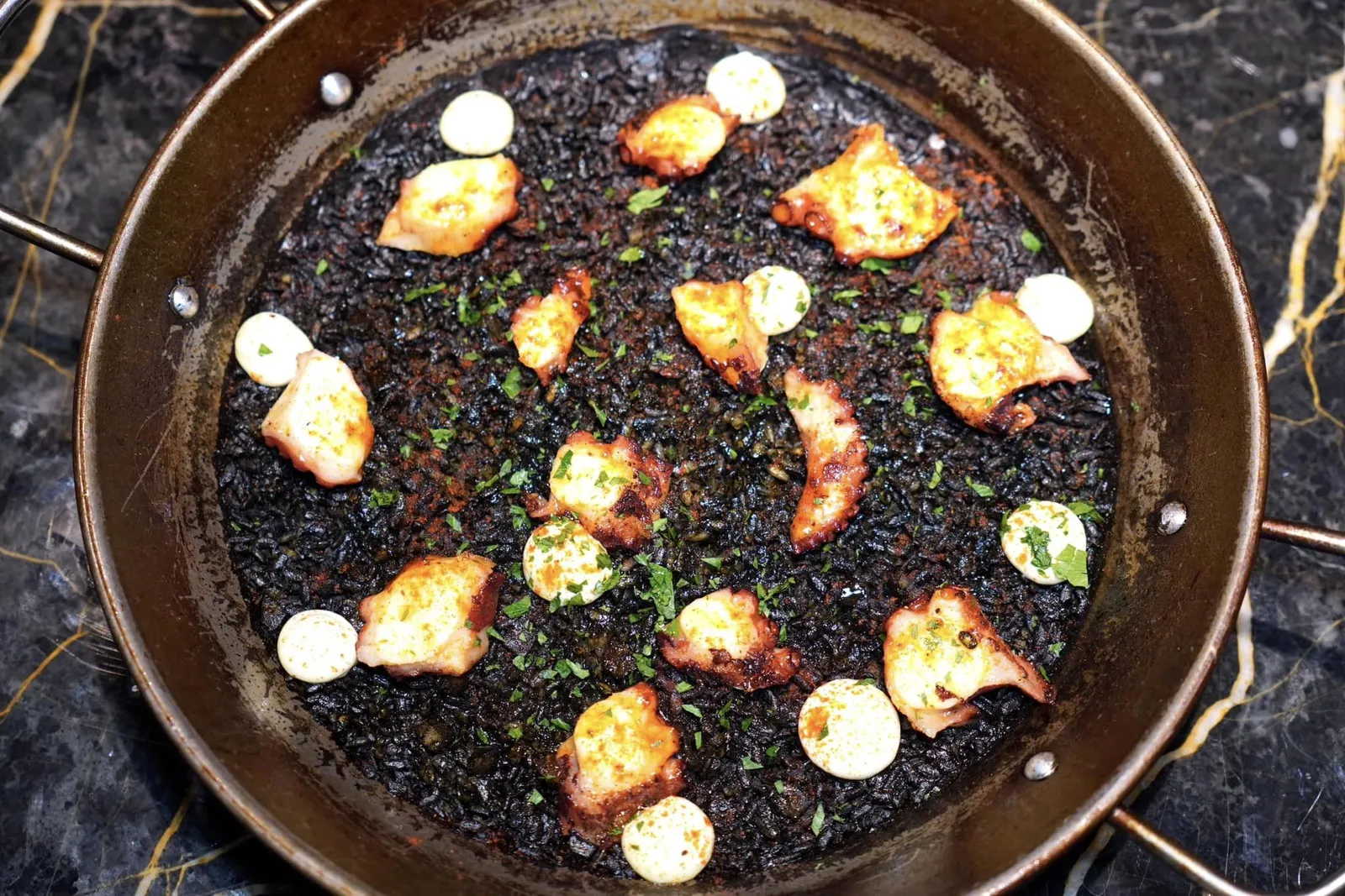 Tako Squid Ink PaellaSquid ink paella topped with Japanese octopusปาเอญ่าเสิร์ฟมาในกระทะขนาดกลางสำหรับแบ่งกันได้ 2 คน เชฟนำดีหมึกไปคลุกกับข้าวก่อนจะนำไปหุงบนเตาฟืนจนสุกกำลังดี เมล็ดข้าวมีความ Socarrat ใช้ได้ ฟเติมแต่งด้วยซอส Aioli ที่ปรุงรสด้วยปาปริก้าและเลมอน (13/20)