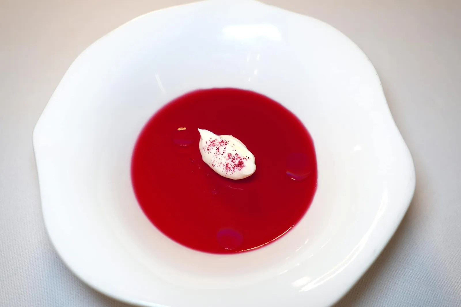Pre-dessertล้างปากด้วย Hibiscus Jelly เสิร์ฟมากับ Almond Oil จำนวน 3 หยด องค์ประกอบสีขาวคือซอสนมวัวโรยด้วยผง Hibiscus