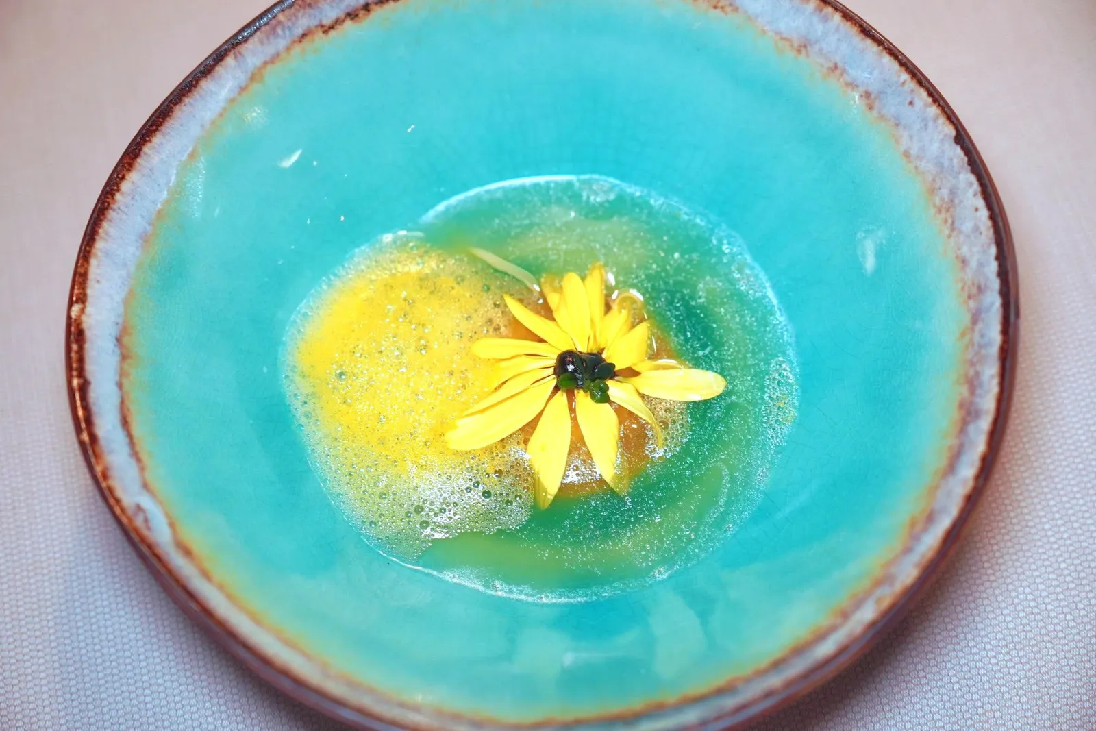 The sun of marigoldBrown trout raviolo with fermented garlic and marygoldRye and spelt sourdough bread, butter from „Schützhof“, pine oilราวิโอโลชิ้นโต ด้านในสอดไส้ปลา Brown Trout ด้านบนและด้านล่างมีด้วยเจลกระเทียมดำหมักและกลีบของดอก Marigold ข้าง ๆ กันคือโฟมที่เตรียมมาจาก Lemon Thyme และปลา Brown Trout (17/20)