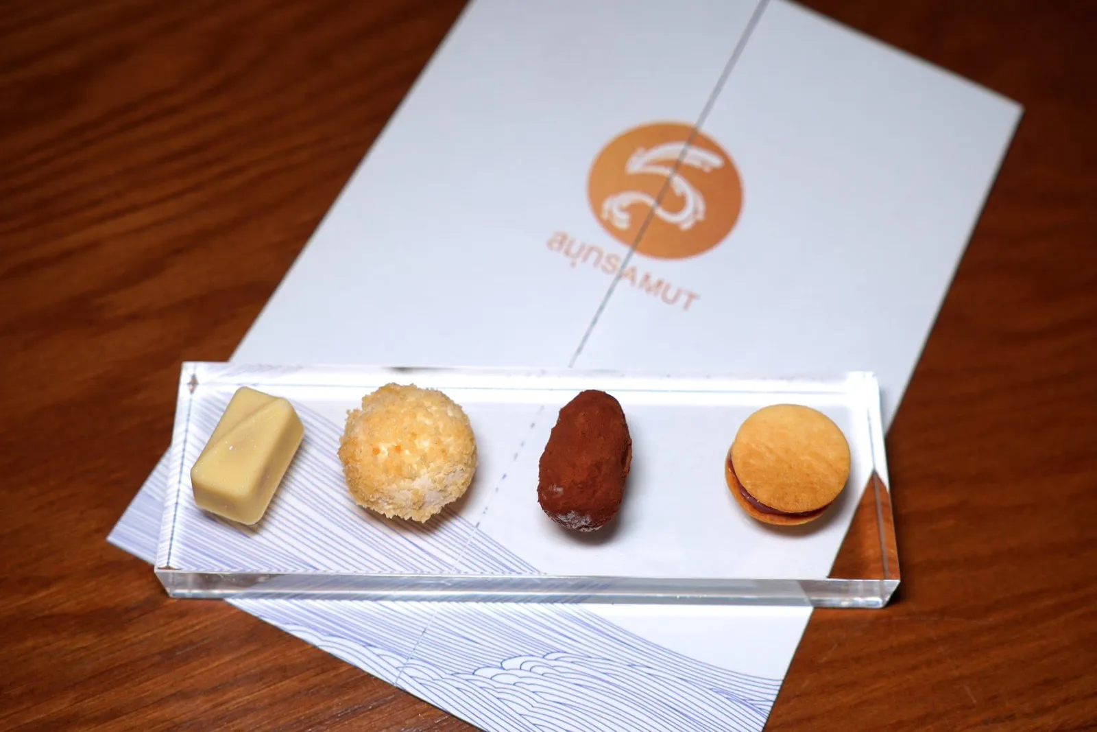Petit-foursปิดท้ายด้วยขนมจิ๋วสี่อย่างคือเกลือเคยไวท์ช็อกโกแลตจากจากฟาร์มไร่ ณ รักษ์ ด้านในสอดไส้เกลือเคยที่ผสมกะปิ เนยถั่ว และแยมสับปะรดเข้าด้วยกัน ถัดมาคือทุเรียนครีมชีส ชิ้นที่สามคือโกโก้ชุมพรสอดไส้เมล็ดมะม่วงหิมพานต์และกาแฟ ด้านนอกคลุกด้วยผงโกโก้ สุดท้ายคือขนมผิงประกอบแยมฝรั่งสีชมพูเอาไว้อีกทีหนึ่ง