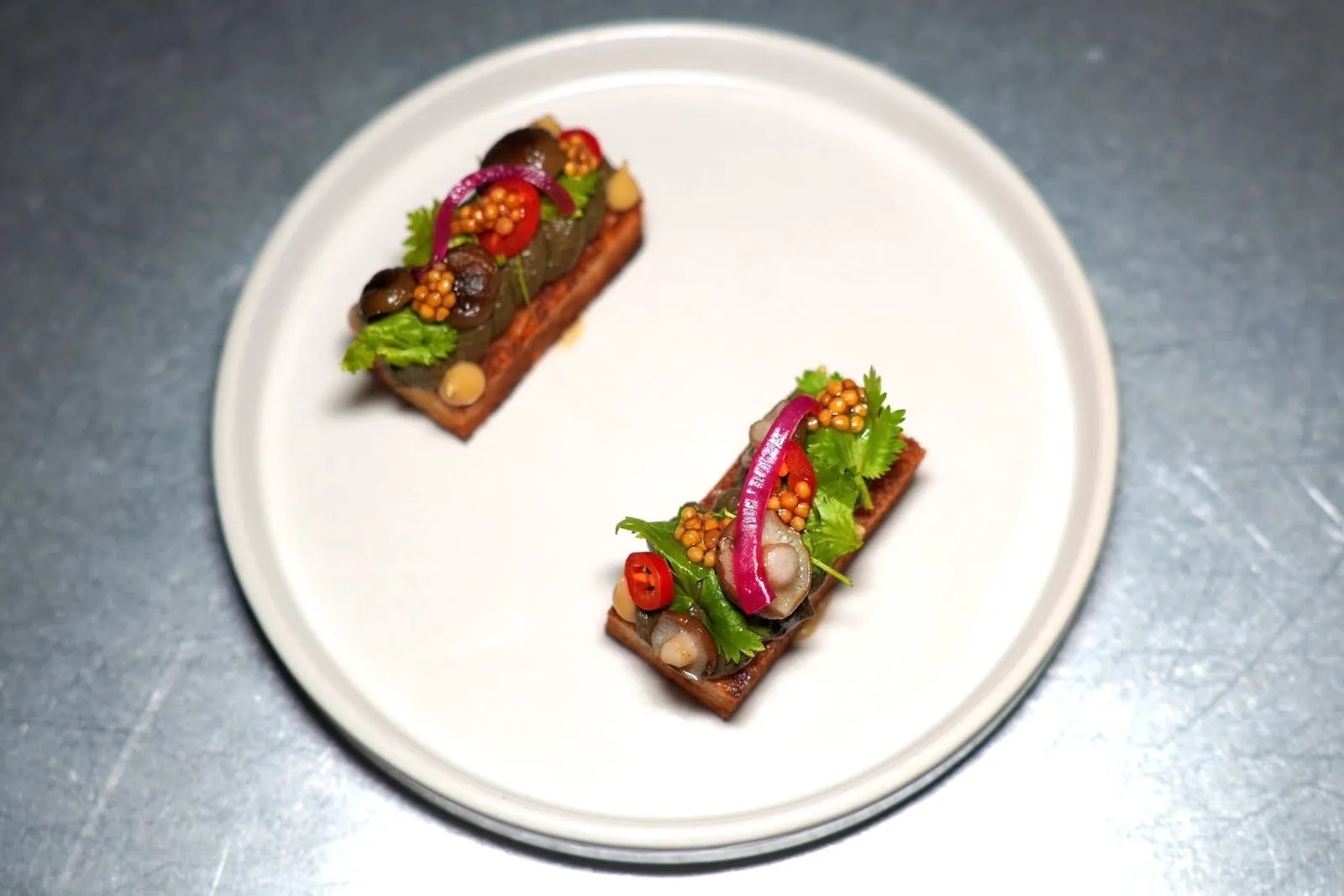 MUSHROOM TOAST (290++)โทสต์เห็ดได้รับแรงบันดาลใจมาจากหมกเห็ดอีสาน เชฟเสิร์ฟปาเต้เห็ดผสมผสานกับปลาร้าและสมุนไพร ด้านล่างคือโชกุปังกรอบนอกนุ่มใน ด้านบนคือผักดองให้รสชาติเปรี้ยวเพียงเบา ๆ