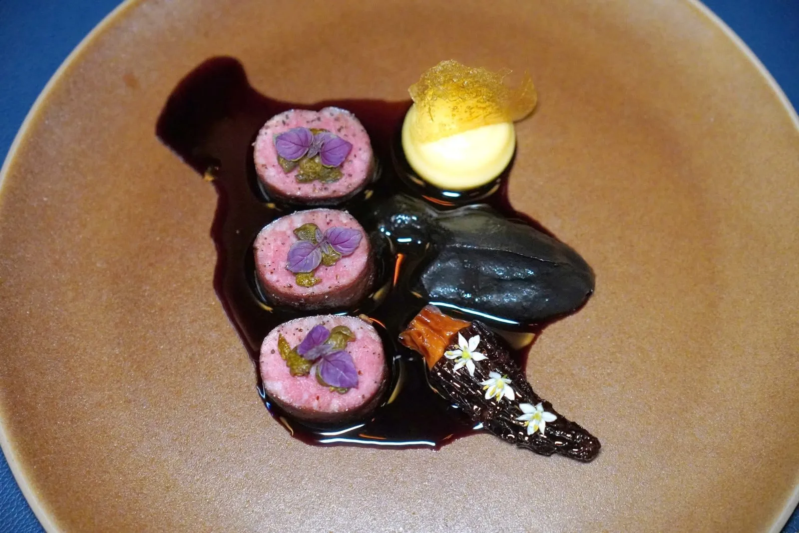 🥄 MAIN COURSECharcoal-Grilled Australian Lamb Striploin, Burnt Eggplant Purée, Madeira Truffle Sauceอีกจานคือเนื้อแกะออสเตรเลียย่างมาสุกพอเหมาะ ท็อปด้านบนด้วยเคเปอร์ทอด ข้าง ๆ กันคือมันฝรั่งบดท็อปด้วยแผ่นกรอบที่เตรียมมาจากน้ำมันฝรั่งเช่นกัน ยังมีเพียวเรที่ได้จากการนำมะเขือไปเผาแล้วปั่นกับหมึกดำ เห็ดมอเรลยัดไส้ด้วยมูสหอยเชลล์ เชฟราดด้วยซอสจูส์ปรุงแต่งรสชาติด้วยน้ำส้มสายชูบัลซามิคเล็กน้อย