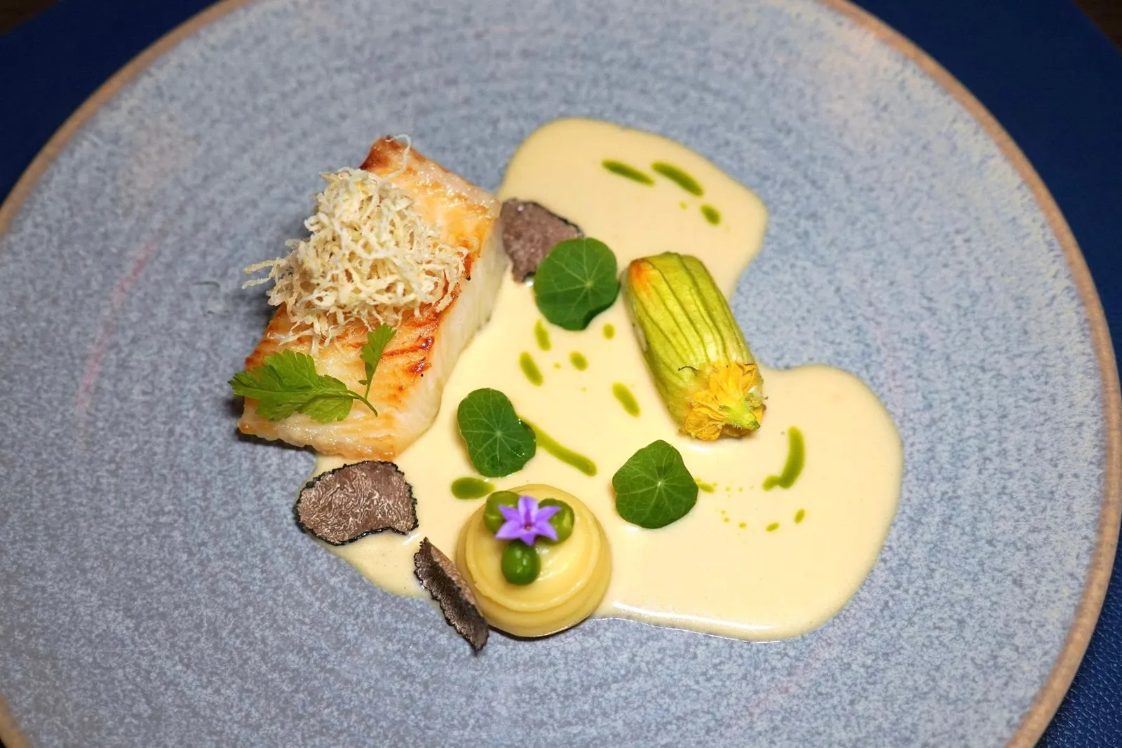 🥄 MAIN COURSECod Fish, Cauliflower Purée, Zucchini Mousseline, Yuzu Beurre Blanc, Fresh Truffleปลาหิมะที่แพนเซียบนกระทะจนสุก ด้านบนคือใบกระเทียมต้นทอดกรอบ ข้าง ๆ กันคือมันฝรั่งบดเนื้อเนียนจับคู่มากับถั่วผัดเนย ซอสรอบ ๆ คือยูซุเบลอบล็องก์ นอกจากนี้ยังมีดอกซูคินียัดไส้มูสหอยเชลล์อยู่ด้วย