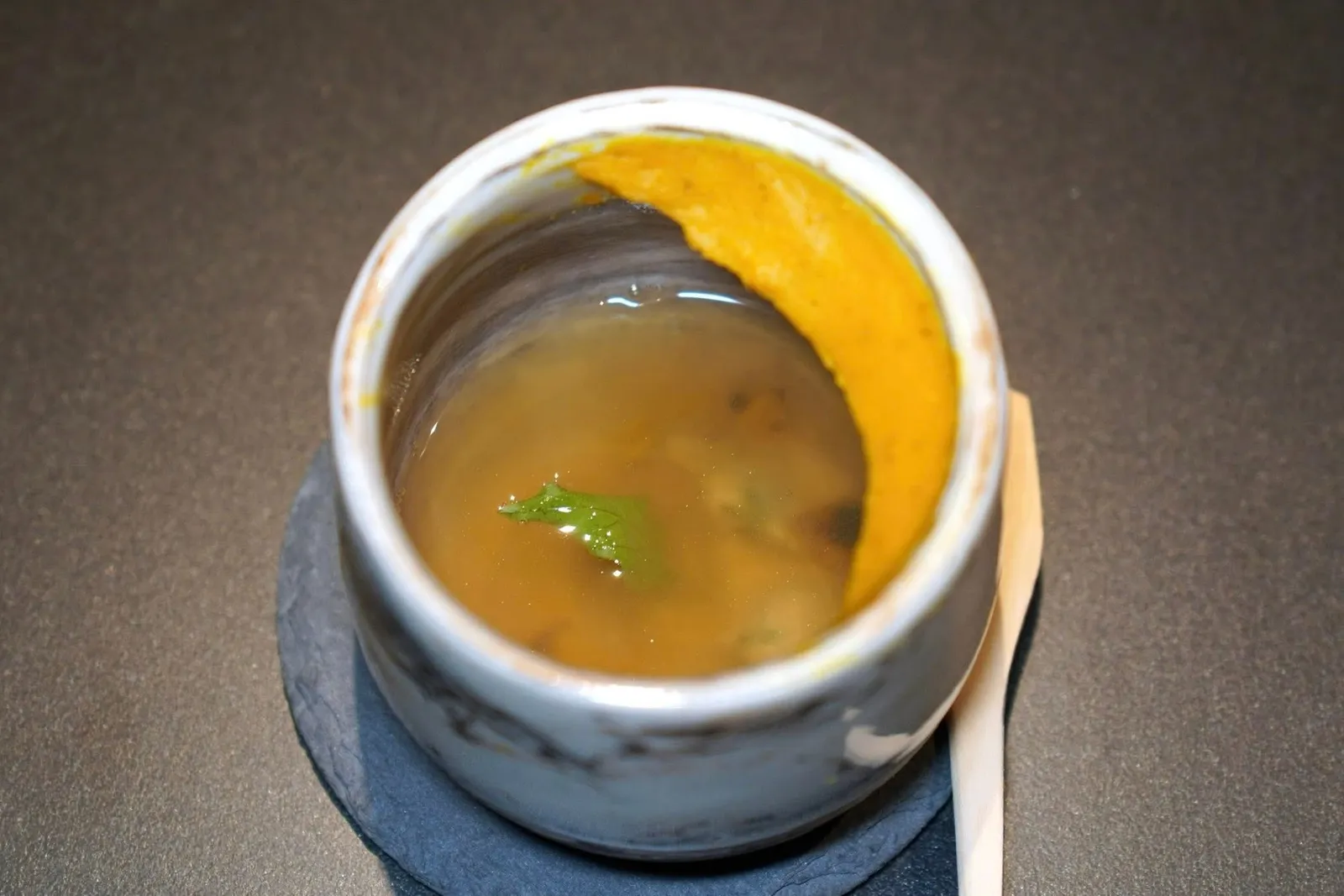 เริ่มต้นด้วย Welcome Drink แบบอาหารคาวโดยเตรียมน้ำซุปมาจากไก่ หมู ปลาช่อนทะเลแห้งจนได้รสชาติกลมกล่อม ด้านล่างมีหอยตลับรมควัน ส่วนรอบ ๆ ขอบแก้วคือฟักทองที่ผ่านการเผาแล้วบดจนละเอียด