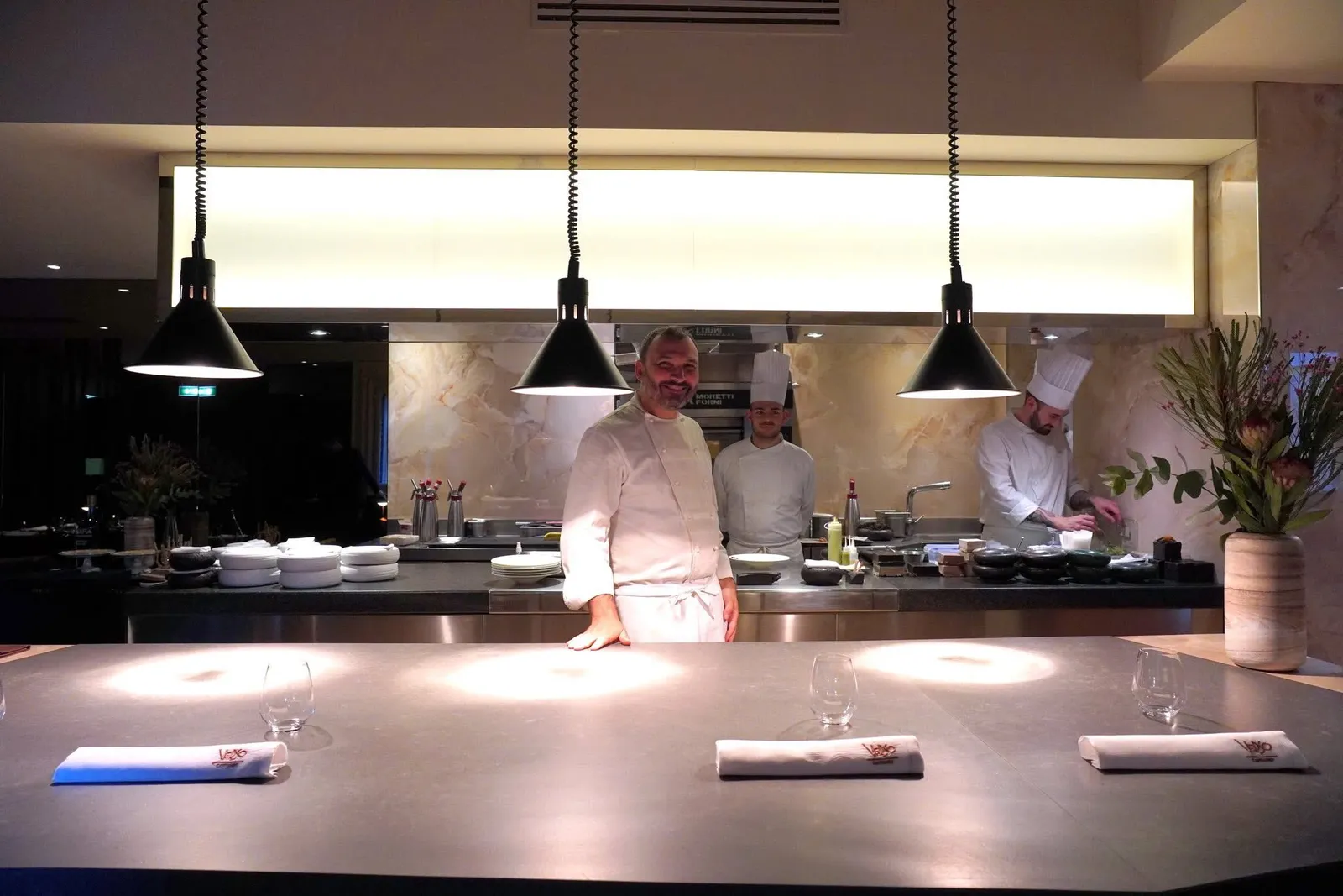 บริษัทออกแบบภายใน Andrea Langhi design จัดวางเคาน์เตอร์ Chef’s Table พร้อมกับครัวเปิดขนาดใหญ่ทำให้ลูกค้าสามารถชมทีมเชฟจัดเตรียมอาหาร แต่งจาน และจัดเสิร์ฟให้ด้วยมือของตัวเอง เบื้องหน้าเป็นโคมไฟสำหรับอุ่นอาหารและส่องสว่างไปพร้อม ๆ กัน
