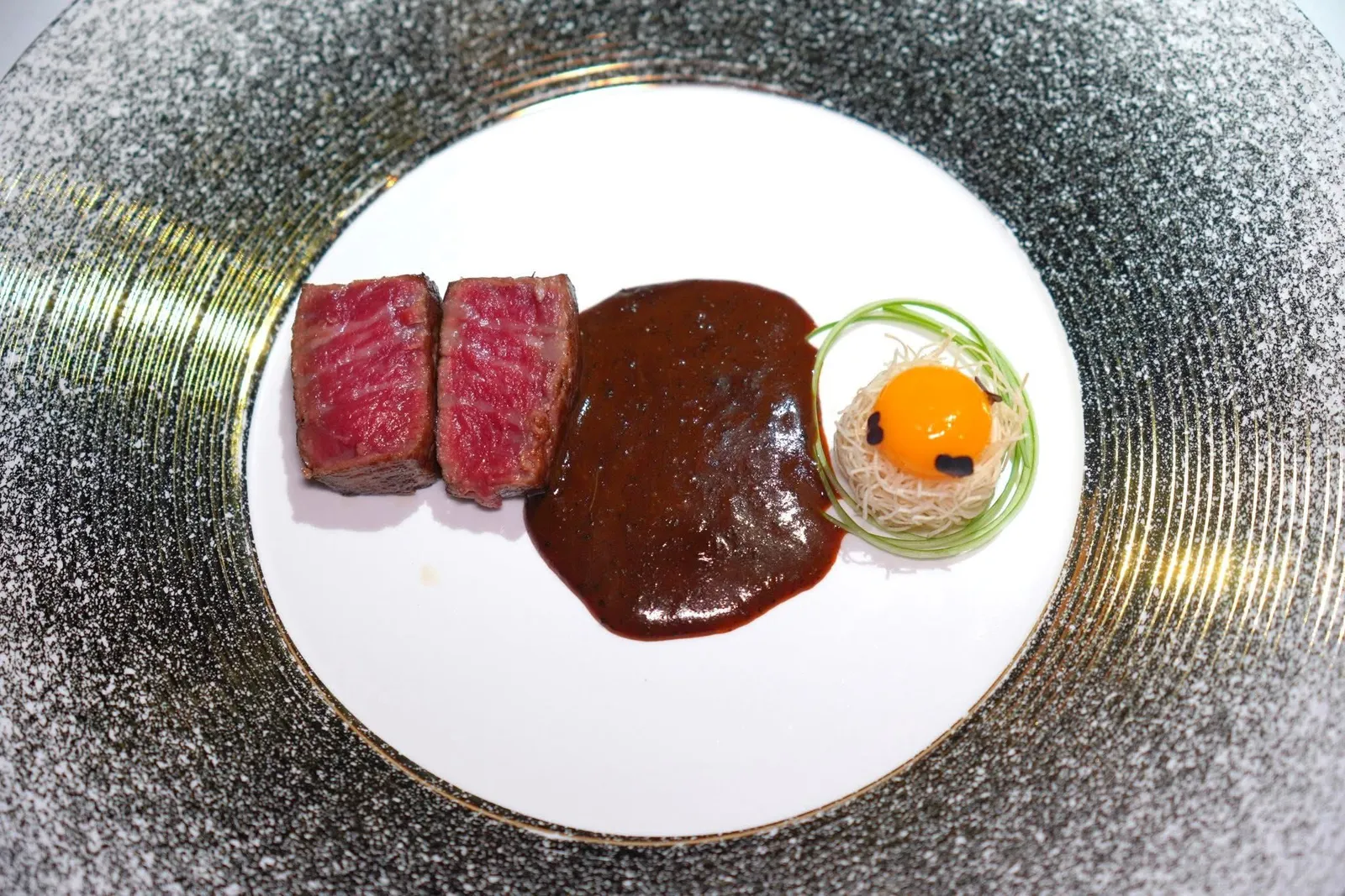 Dry Aged A5 Wagyu Beef熟成A5和牛เมนูนี้เชฟได้รับแรงบันดาลใจมาจากตลาดกลางคืนในไต้หวันซึ่งมีเมนูเนื้อย่างที่พบได้อยู่บ่อย ๆ ในจานนี้เชฟเลือกใช้เนื้อวัววากิวระดับเอ 5 ส่วนเทนเดอร์ลอยน์ที่ผ่านการดรายเอจนาน 30 วัน รอบ ๆ คลุกด้วยหมาล่าไต้หวัน จากนั้นเสิร์ฟมากับซอสที่ผสมผสานซอสเอวัน (A.1.) เข้ากันกับซอสพริกไทยดำ มะเขือเทศ หอมแดง และหัวหอมใหญ่ ข้าง ๆ กันคือเส้นหมี่กรอบท็อปด้วยไข่นกกระทา (14/20)