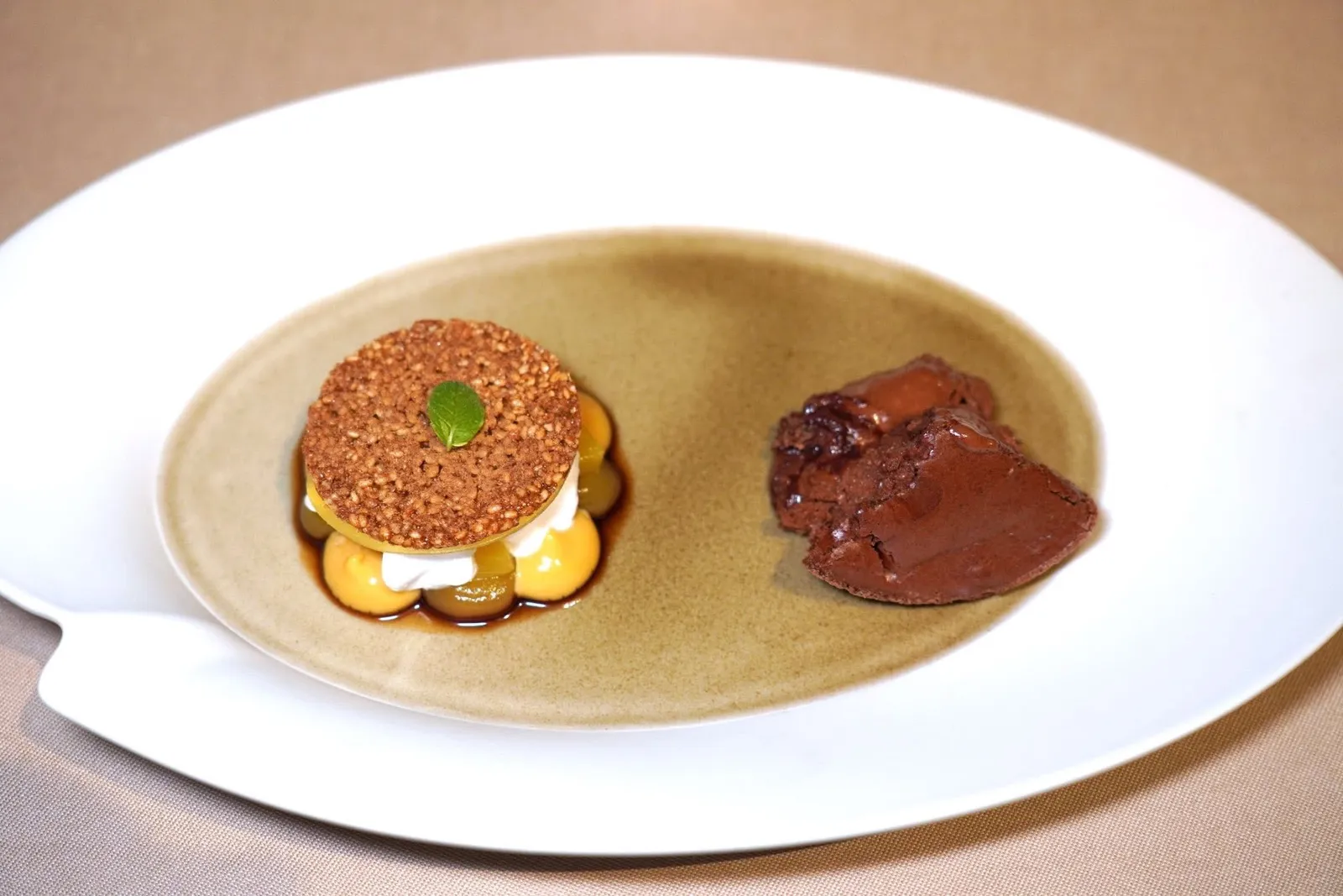 Guanaja chocolate soufflé, salted peanut, rum pineapple, coconut vinegar and toasted sesameซูเฟล่ที่เตรียมมาจากช็อกโกแลต Guanaja เสิร์ฟมาร้อน ๆ เนื้อซูเฟล่นุ่ม ฟู หอม รสชาติเข้มข้น ผิวชั้นนอกมีความกรอบเบา ๆ ด้านล่างของซูเฟลแอบซ่อนคือ Hot Peanut Heart หรือหัวใจถั่วลิสงเอาไว้ด้วย ในจานมีองค์ประกอบของสับปะรดและเหล้ารัมจับคู่กับครีมงาคั่ว ยังมีไอศกรีมนมแพะที่มีอโรมาของพริกไทยและโฟมน้ำส้มสายชูมะพร้าว ด้านบนคือชิ้นสุดท้ายคือแผ่นกรอบที่เตรียมมาจากงาคั่วนั่นเอง (19/20)