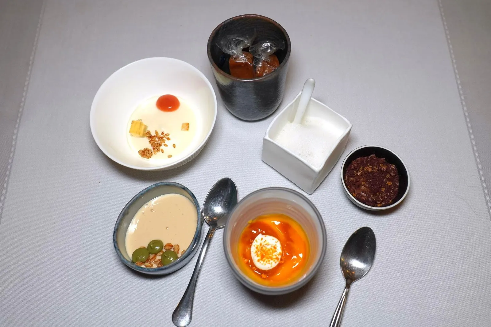 Mignardises like a Pan Massala - Game of Texturesของหวานจิ๋วประกอบไปด้วย Rice cake with milk, Sicilian Pistachio and puffed spelt ถ้วยกลมสีขาวคือ Guava condiments with sesame seed, Armagnac jelly and yuzu ถ้วยล่างคือ Mango with turmeric almond ในถ้วยขาวสี่เหลี่ยมคือ Lemon from Menton with Matcha ถ้วยขวามือคือ Grand Cru chocolate with Pienmont hazelnut and corn ปิดท้ายด้วยท็อฟฟี่ Caramel with Sarasin