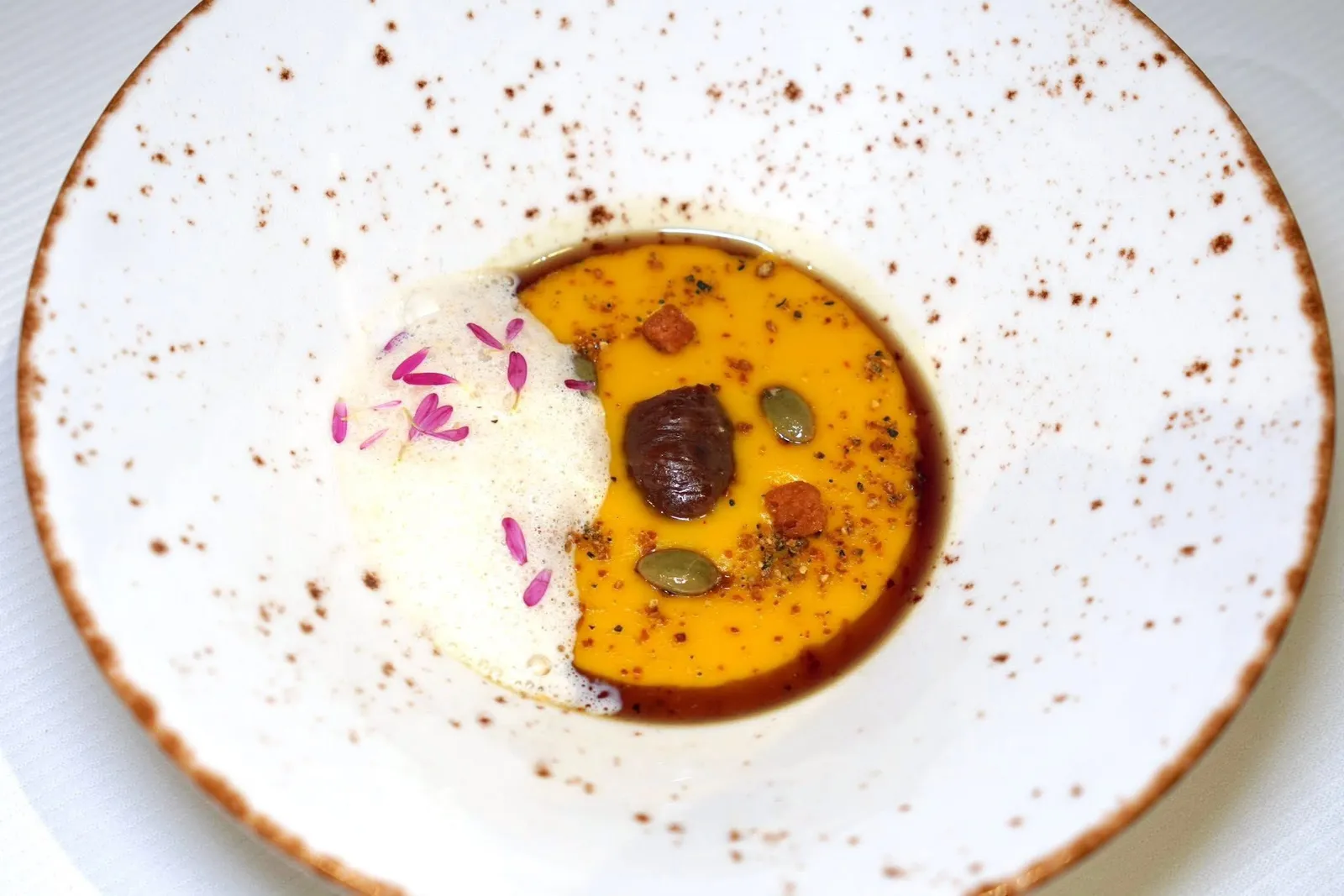 Amuse BoucheButternut Soup I Chestnut ice cream | parmesan Emulsion | Calendulaด้านบนท็อปด้วยองค์ประกอบของเกาลัดสร้างรสหวาน ครูตองกรอบ และเมล็ดฟักทอง รอบ ๆ คือน้ำมันเกาลัด จากนั้นพนักงานจะตักอีมัลชั่นโฟมชีสพาเมซานและดอก Margeret สีม่วงเสริมรสชาติฝาดเพียงเล็กน้อยลงไปในจาน (16/20)