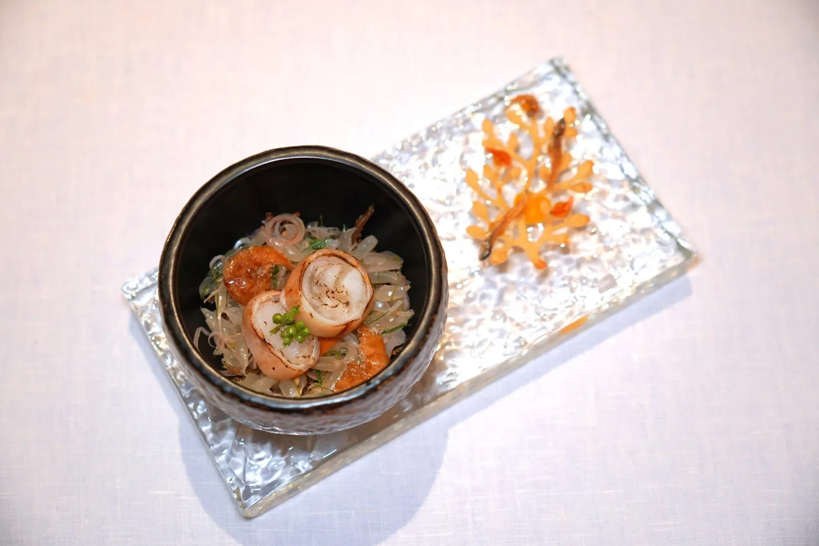 Pomelo Salad with Sun-Dried Squid Roe and Crispy SeafoodPomelo | Sun-Dried Squid | Housemade Dressing | Crispy Seafood“ยำส้มโอเครื่องกรอบ ปลาหมึก ไข่ปลาทะเล” เป็นเมนูที่เชฟเสิร์ฟยำส้มโอช่วยเรียกความสดชื่นโดยใช้ส้มโอขาวใหญ่ GI จากอัมพวาให้ความหวานและฉ่ำ ในจานยังมีปลาหมึกไข่จากปราณบุรี รสชาติมีความจัดจ้านจากมูสน้ำยำสูตรบ้านบุณยาคม เครื่องกรอบของจานประกอบไปด้วยกุ้งแห้งกรอบ เมล็ดมะม่วงหิมพานต์ และหอมแดงเจียว อีกฝั่งคือแผ่นปะการังกรอบที่เตรียมมาจากน้ำมันหอมเจียวท็อปด้วยปลาจิ้งจั้งนั่นเอง (14/20)