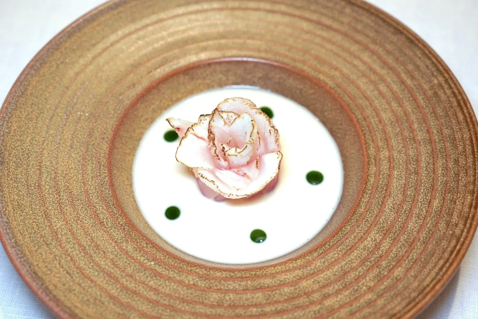 Dry-Aged Fish with Tom-Kha Cold SoupWhite Fish Dry Aged | Galangal | Cilantro Oil | Coconut Milkเมนูที่เชฟใช้ชื่อว่า “ปลาสามเกลอ ซอสต้มข่า” ได้จากการปลากุดสลาดแดงถึง 3 ส่วนคือเนื้อปลาที่ผ่านกระบวนการ Dry-aged วางเรียงมาเป็นรูปดอกไม้สวยงาม เนื้อปลามีความหนึบแต่ไม่เหนียว นอกจากนี้ยังมีกระดูกและหัวปลาที่เชฟนำไปเคี่ยวทำมาเป็นซุปต้มข่าที่เต็มไปด้วยคอลลาเจนและมีรสชาติกลมกล่อม เชฟตัดเลี่ยนด้วยความฉุนเบา ๆ ของน้ำมันผักชีฝรั่งที่ผ่านกกระบวนการรมควันเย็นด้วยไม้เอลเดอร์ (15/20)