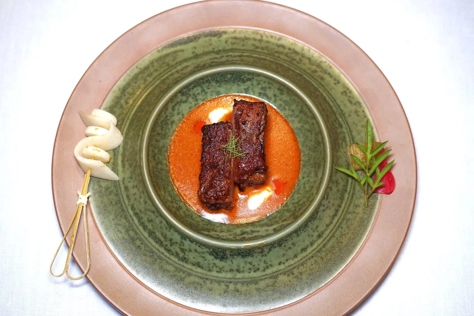 Beef Panang with Kra-Bok RiceLias-gyu's beef | Panang Curry | Eggplant | Kra-Bok Riceตัวแกงมีเนื้อสัมผัสเนียน รสชาติและอโรมาของเครื่องเทศเข้มข้น ข้างจานฝั่งหนึ่งคือยำขาวที่ได้จากการนำมันแกวและแห้วมายำกับน้ำสะเออะปรุงสุก อีกฝั่งหนึ่งคือมะเขือยาวย่างดองดาชิ หอมแดงดอง และใบเล็บครุฑลังกา (15/20)